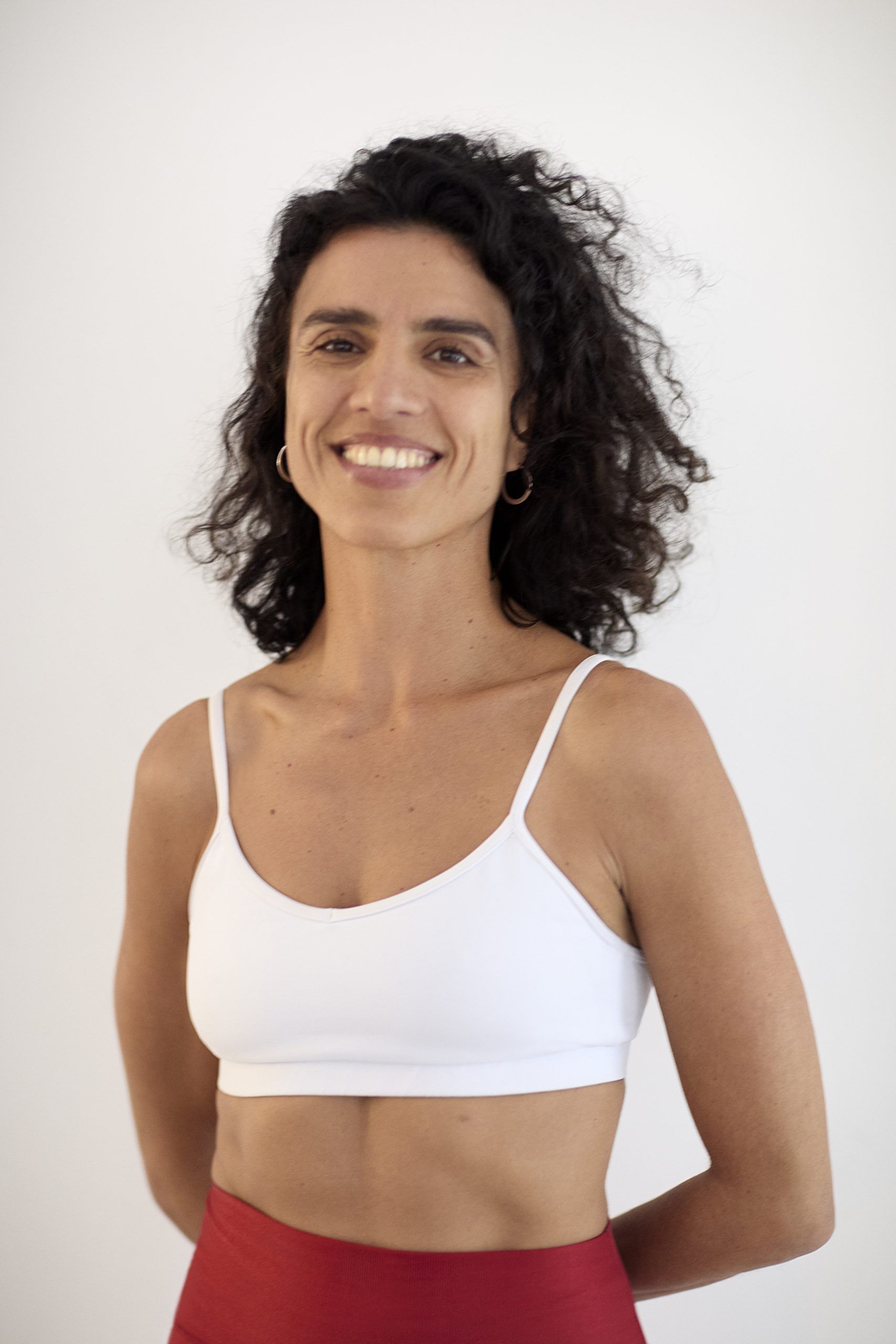 Acro Yoga Teacher Erica Montes wearing a white sports bra and red shorts smiling against a white background