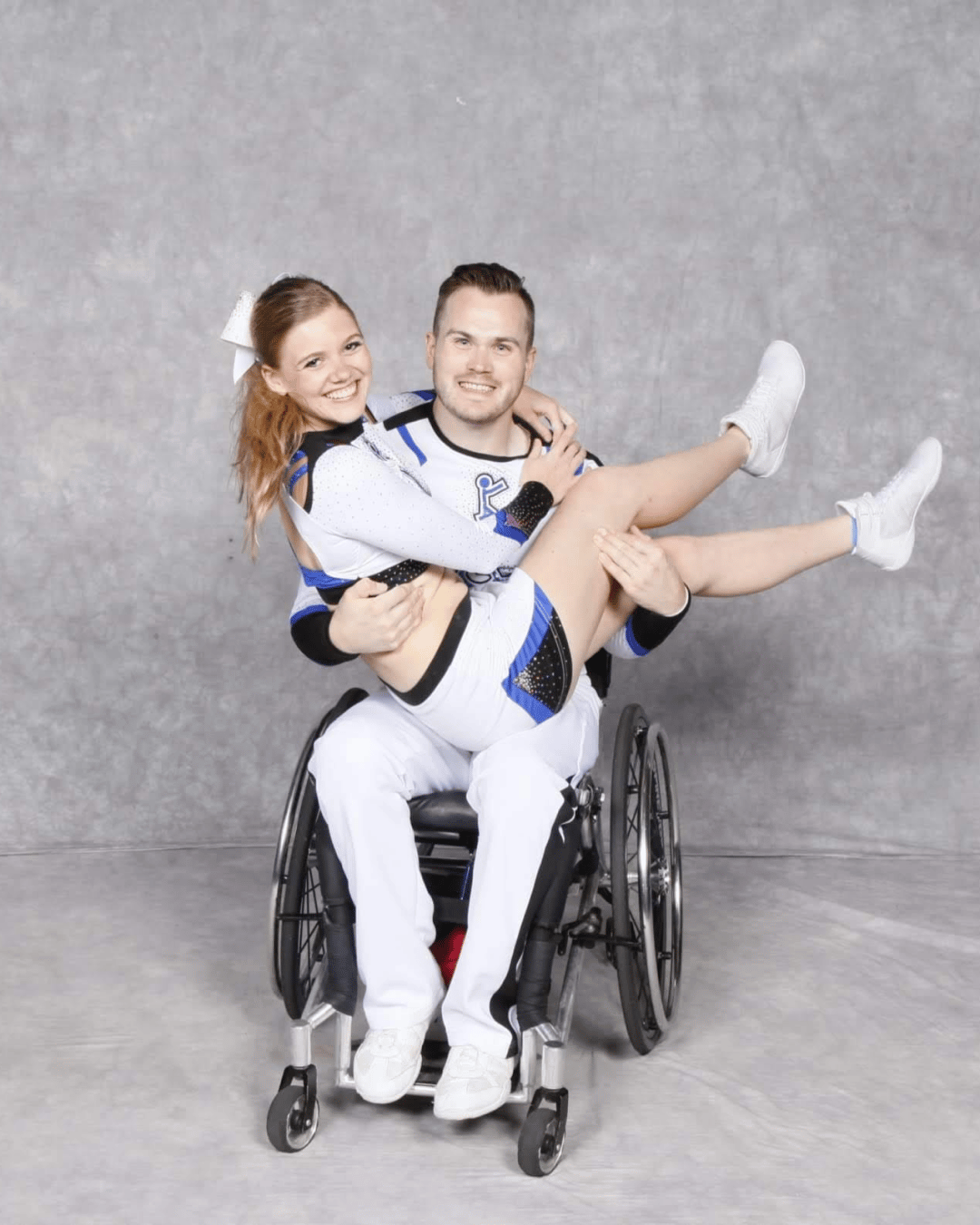 Rick Rogers holding Chantal Epps on his lap both wearing cheerleading outfits