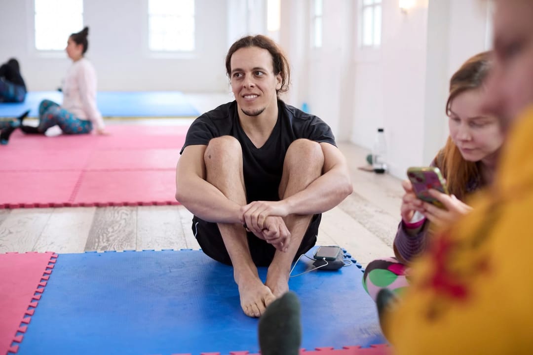 Satori Silva sitting on a blue puzzle mat with his arms wrapped around his legs