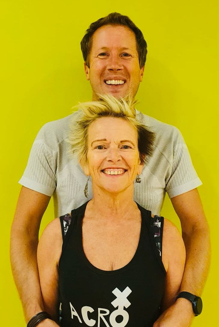 Shena Grigor and Tim Ashworth standing in front of a bright yellow wall and smiling